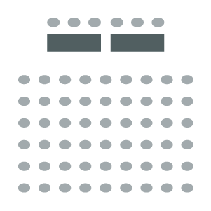 Rows of chairs arranged facing panel table and chairs at front of room.