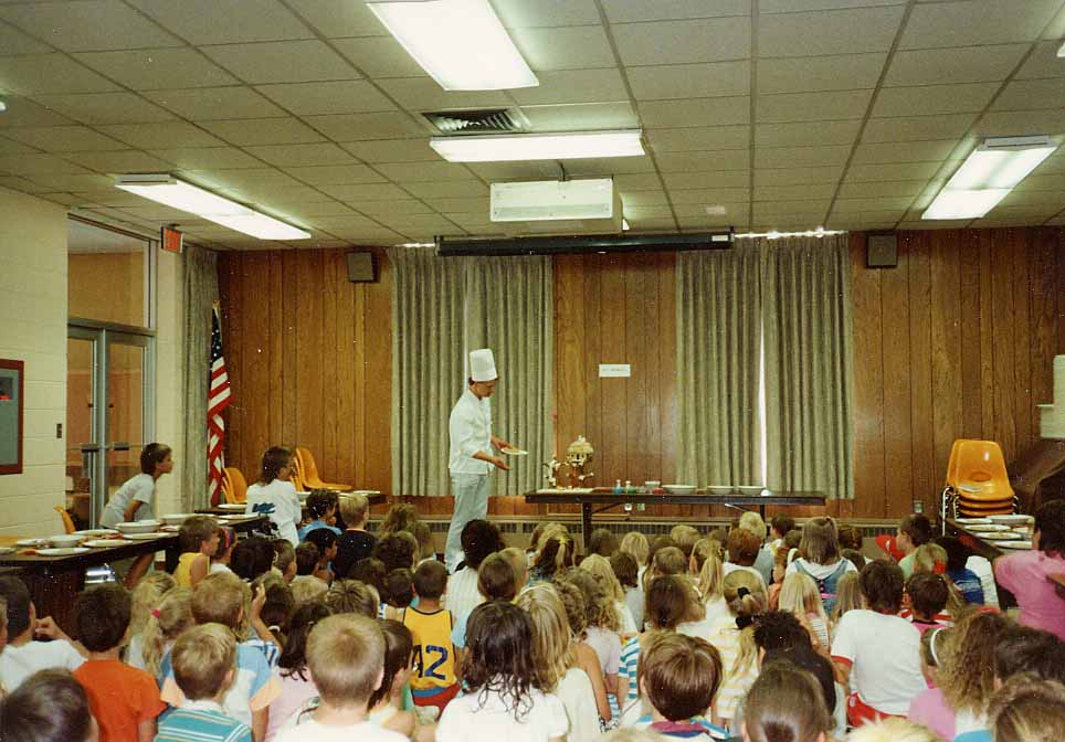 Presenter demonstrates gingerbread construction to crowd of children at a library event