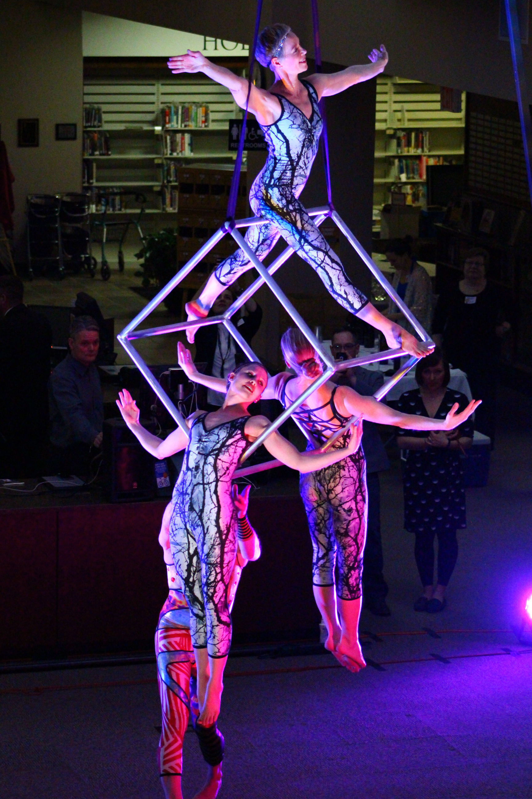 Aerial performers balancing on suspended cube framework