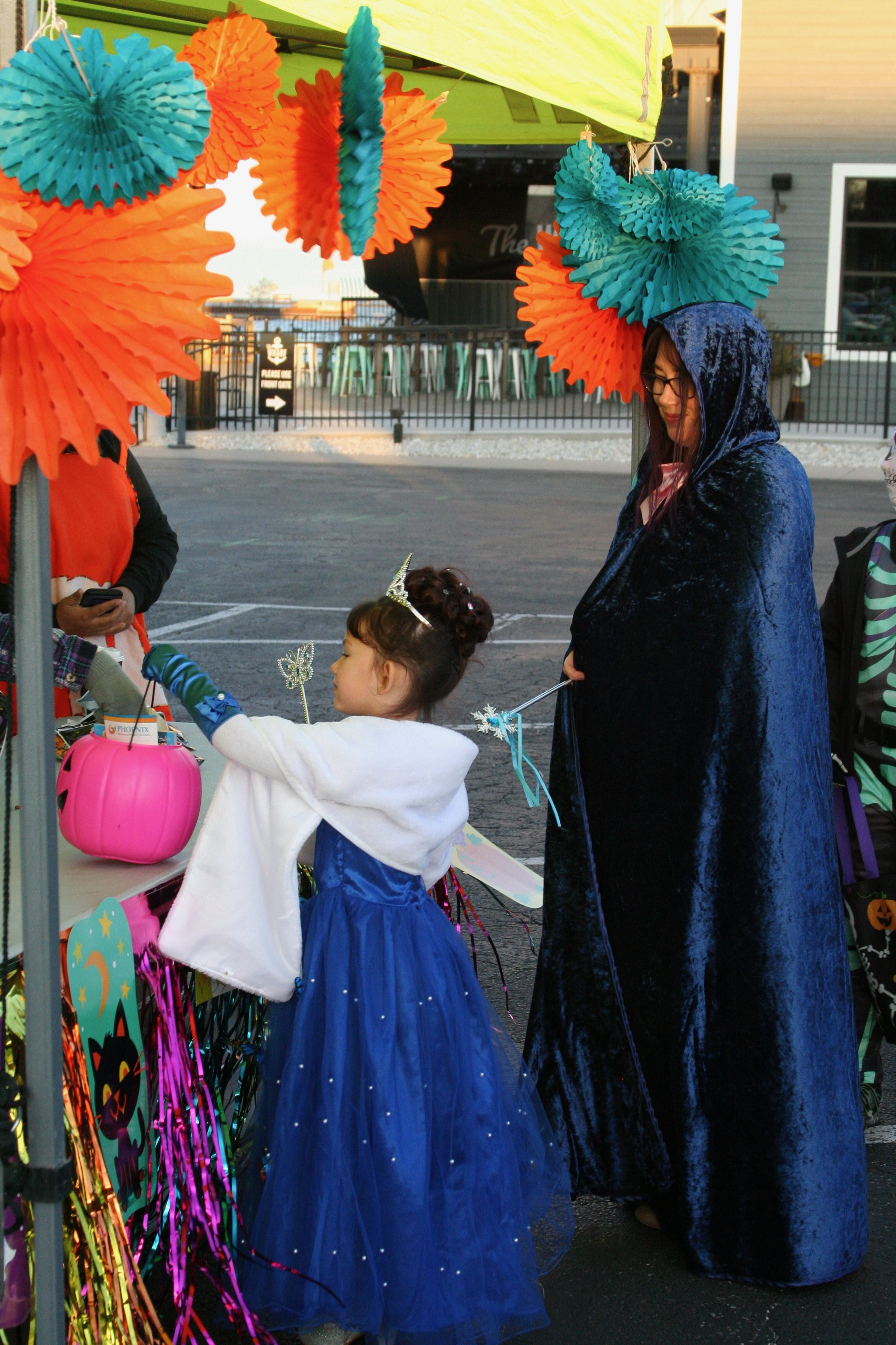Woman wearing cloak and child dressed as princess collecting candy