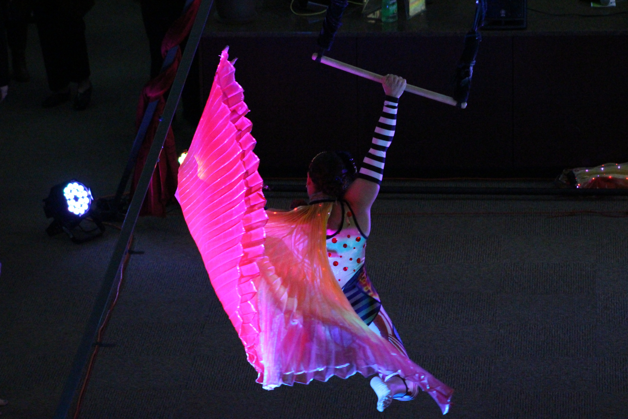 Aerial performer with pink parasol swings from suspended bar