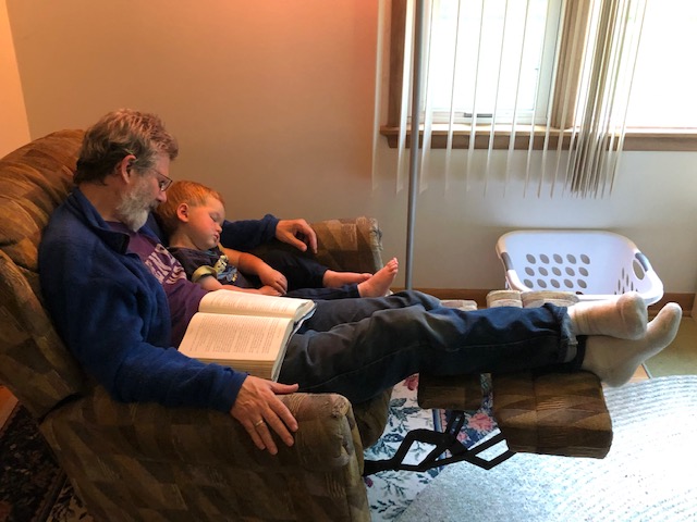 Older man and child asleep in chair with book