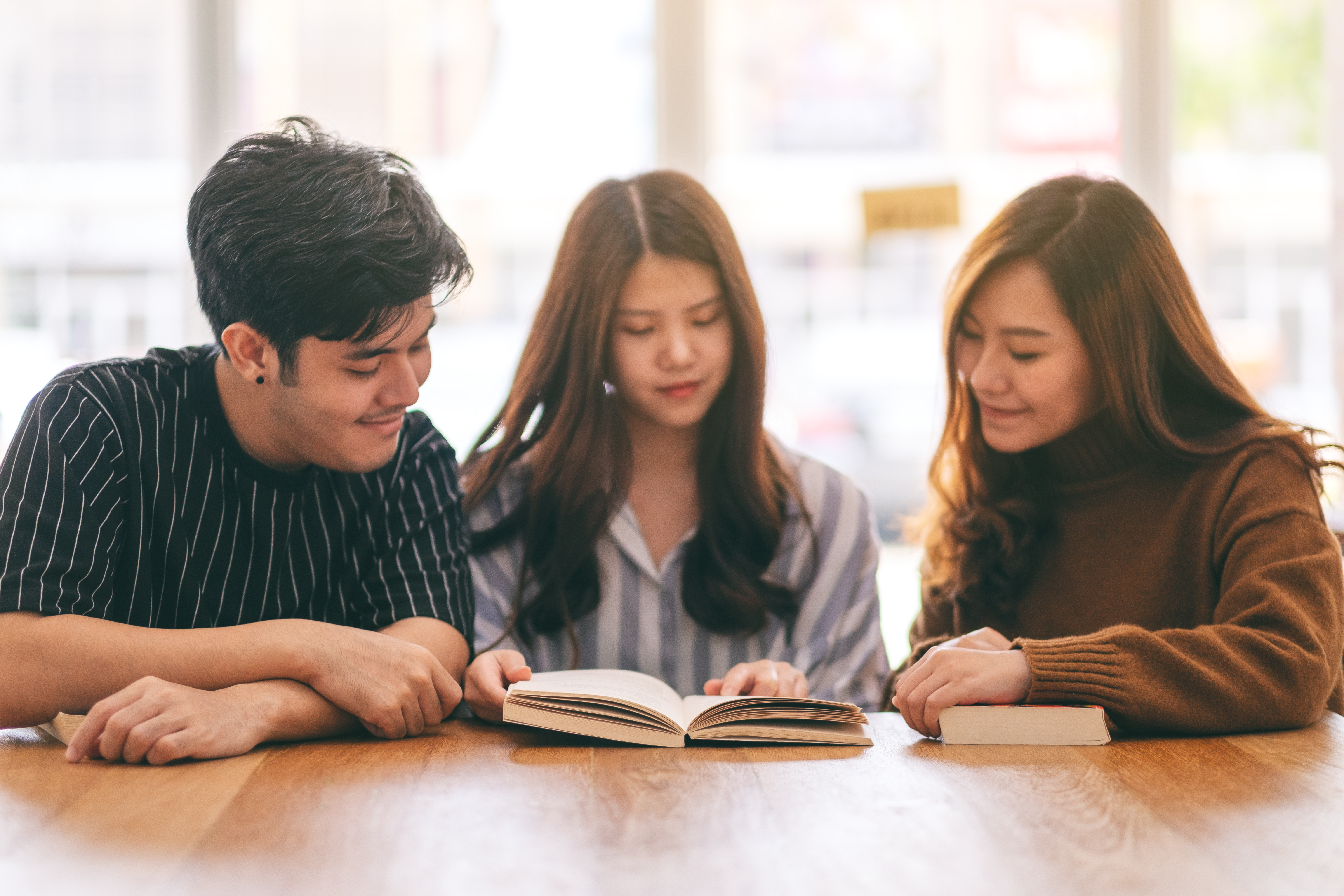 Three teens looking at an open book