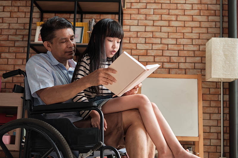 Man in wheelchair with granddaughter on his lap reading a book