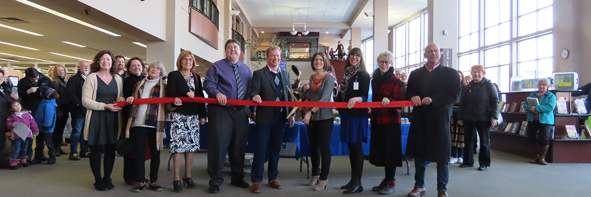 Library Foundation standing and smiling with red ribbon during ribbon cutting ceremony
