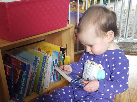 Baby in purple polka dot pajamas reading board books