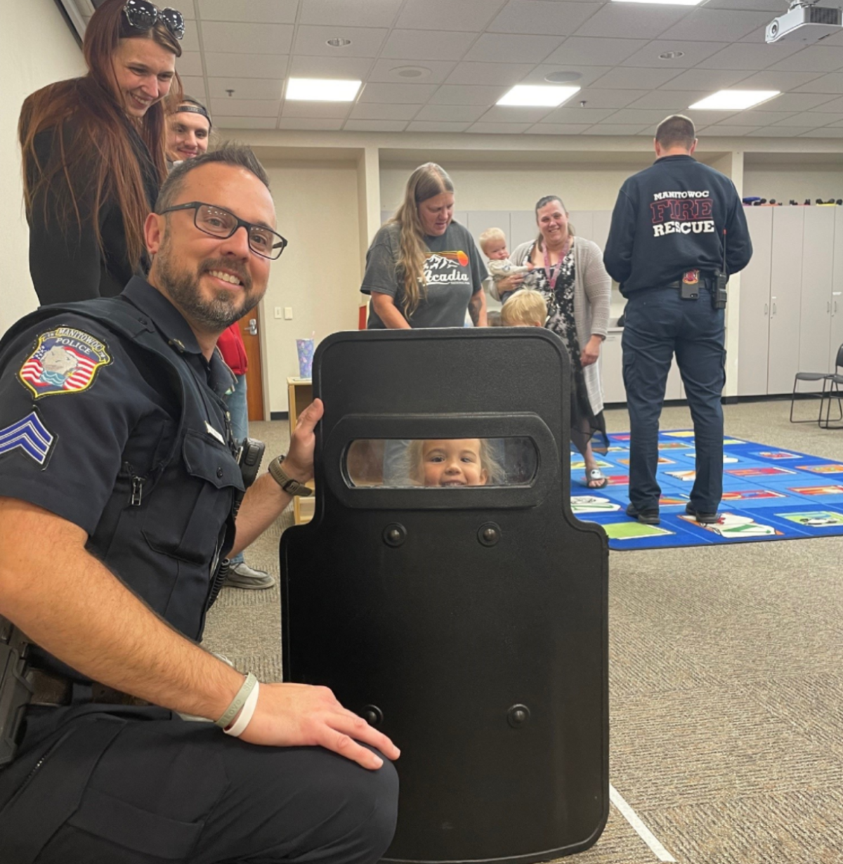 Photo of a police officer with a child hiding behind a shield