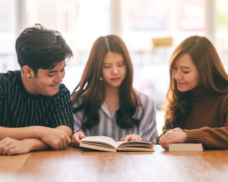 Three teens looking at an open book