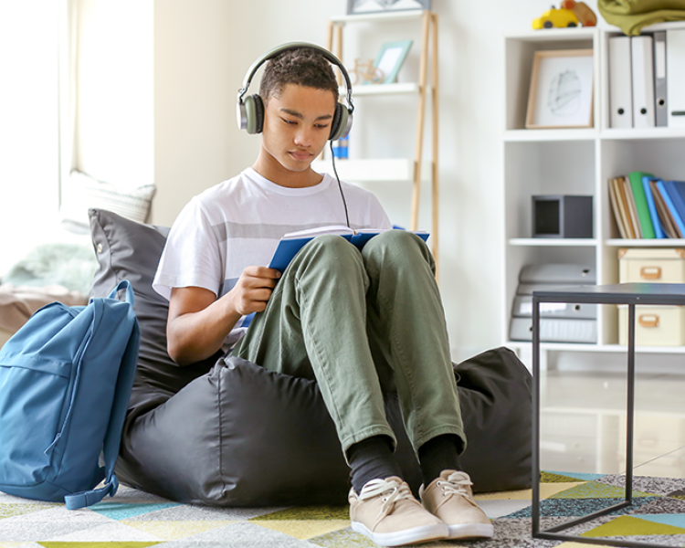 Teen boy sitting in bean bag with book in lap and headphones on
